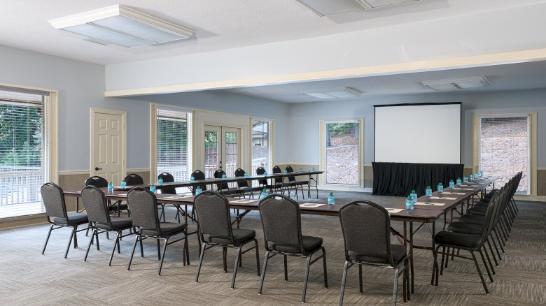 A conference room with a U-shaped table setup, many chairs, a projector screen, and water bottles on the table, ready for a meeting.