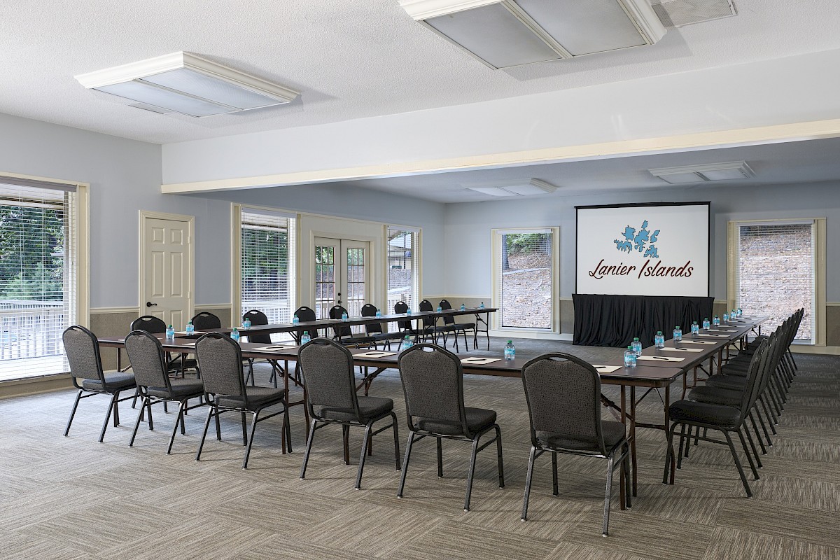 A conference room with a U-shaped table, many chairs, a projector screen displaying “Luther Island” and windows on two sides.