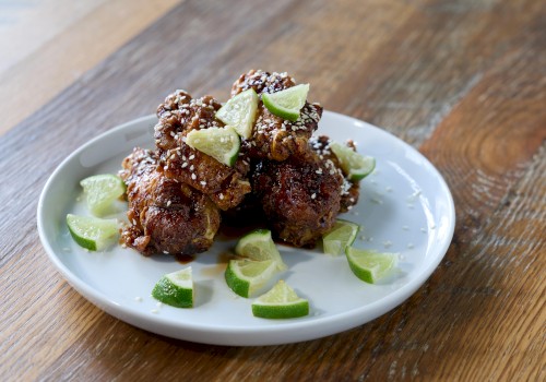 Fried chicken pieces topped with lime wedges, sesame seeds, served on a white plate on a wooden table.