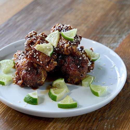 Fried chicken pieces topped with lime wedges, sesame seeds, served on a white plate on a wooden table.