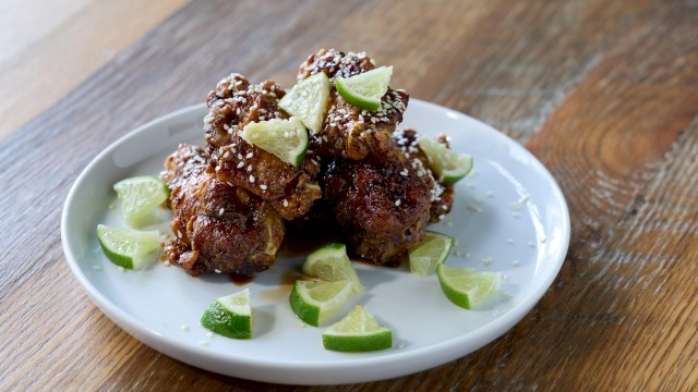 Fried chicken pieces topped with lime wedges, sesame seeds, served on a white plate on a wooden table.