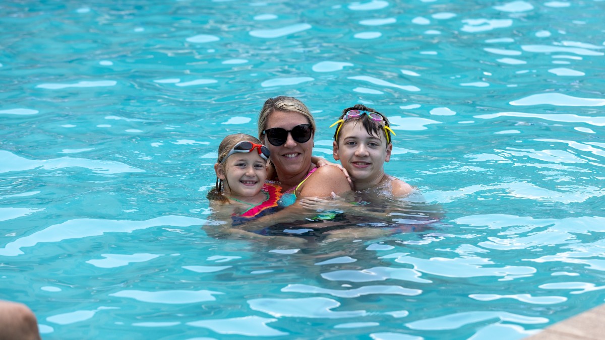 A woman with two children in sunglasses swimming and enjoying in a pool on a sunny day.