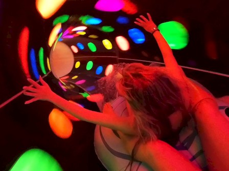 A person is riding an inflatable raft through a colorful, illuminated water slide tunnel with vibrant, swirling lights.
