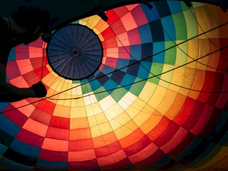 A person prepares a colorful hot air balloon for inflation, with vibrant fabric visible from inside the balloon's envelope.