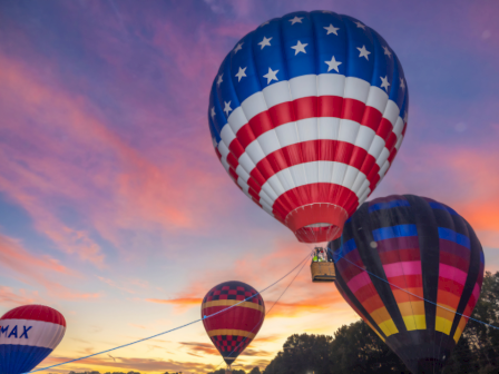 Hot air balloons float during sunset with patriotic American flag design on the main balloon.