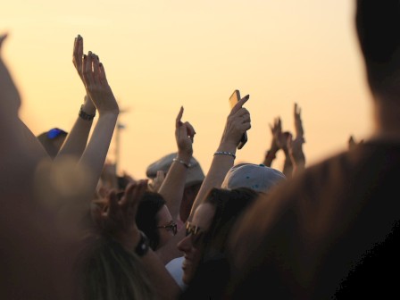 Crowd with raised hands and smartphones at sunset during an outdoor event or concert.