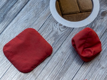 This image shows a wooden table with red sunglasses, two red cloth objects, and a circular hole with a metallic edge, on a brick background.