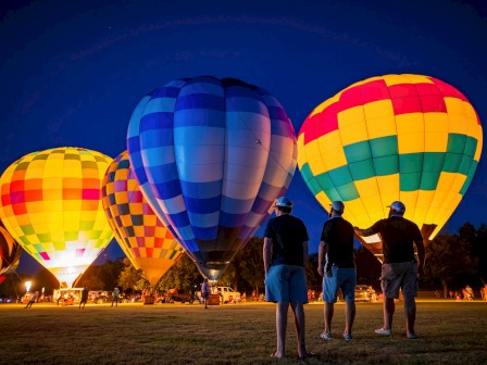 People prepare hot air balloons for a nighttime launch at a festival or event with colorful balloons and spectators.
