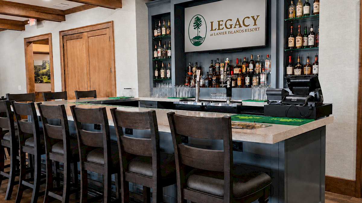 A hotel bar with a blue counter, high chairs, liquor bottles, a TV displaying 
