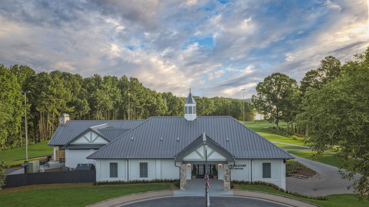 A charming golf clubhouse with a metal roof, surrounded by lush greenery and a scenic sky above.