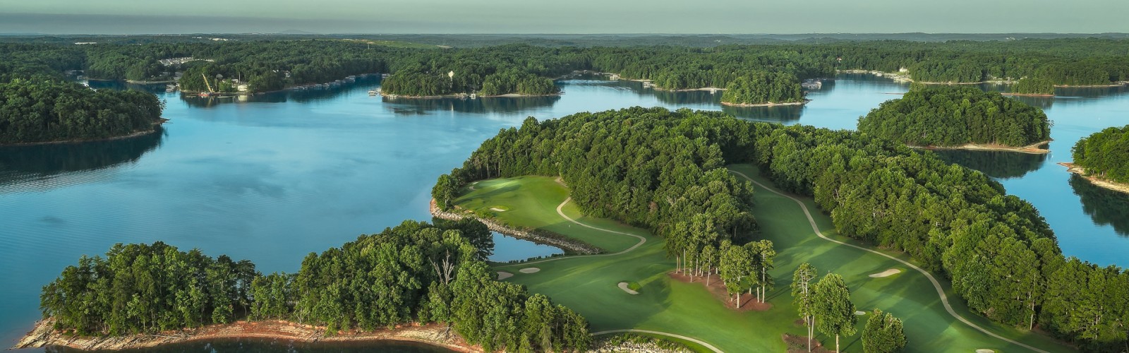 An aerial view of a large lake surrounded by lush forests with a golf course on a small peninsula.
