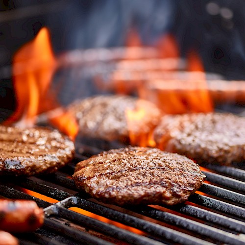 Burgers and hot dogs are grilling on a barbecue with flames rising, creating a classic outdoor cooking scene.