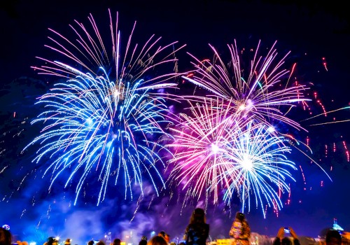A crowd watches vibrant blue and pink fireworks bursting in the night sky.