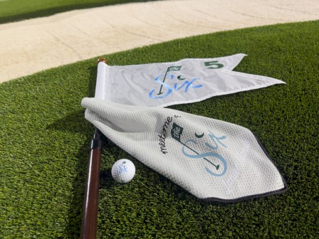 Golf flags, a golf ball, and a golf club on a green, with a message about meeting at 