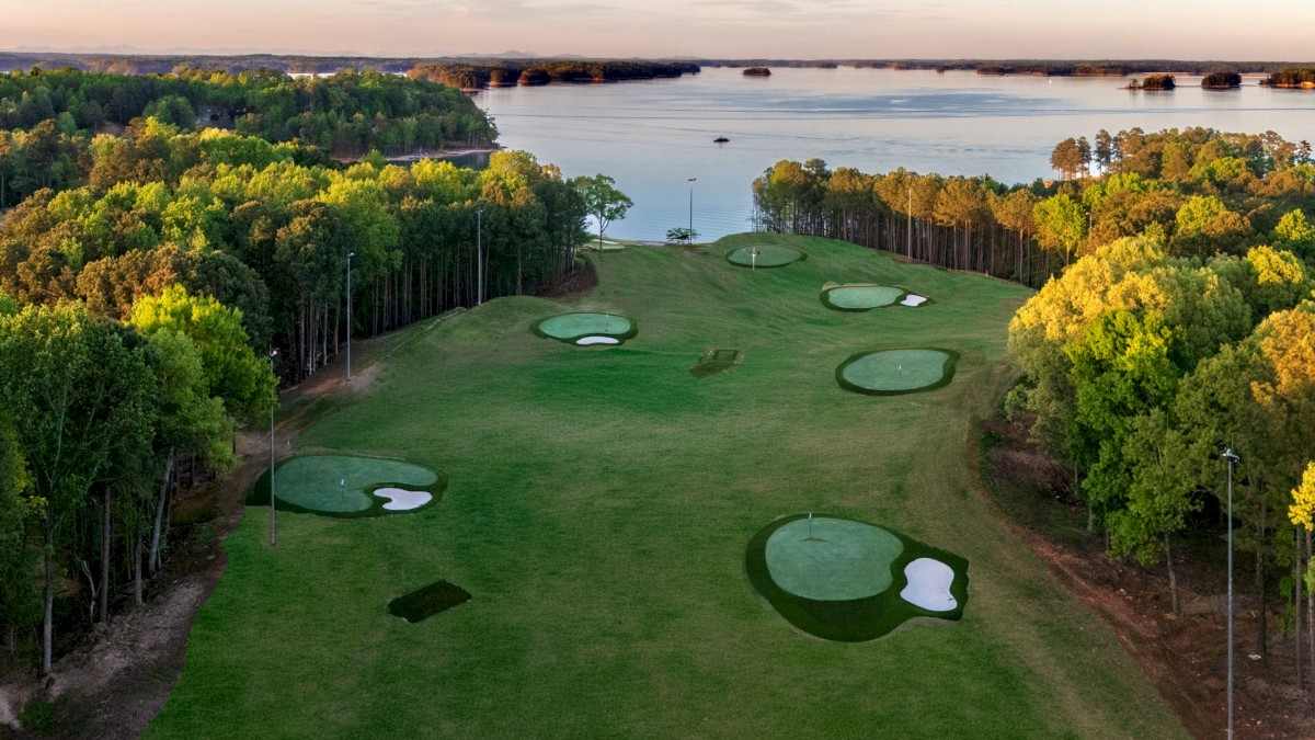 This is an aerial view of a golf course near a large body of water, with trees along the fairways and several sand bunkers.
