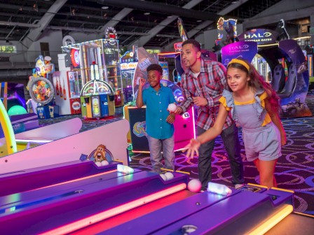 A family plays a skee-ball game in a colorful arcade filled with bright lights and entertainment options.