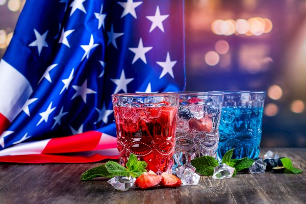 Colorful patriotic drinks with strawberries, mint, and ice in front of an American flag background.