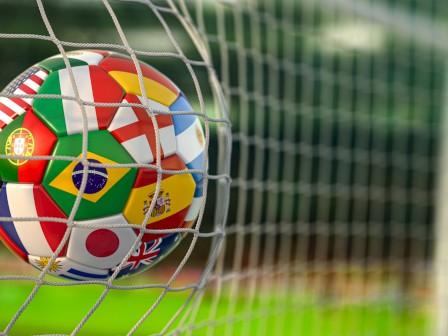 A soccer ball with flags from various countries is in the net at the goal.
