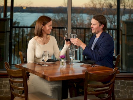 A couple sharing a romantic toast at dinner with glasses of red wine inside a cozy restaurant.