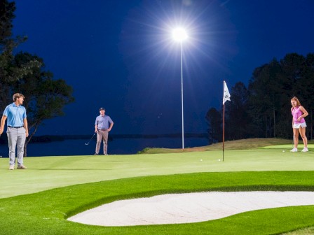 People are playing golf on a putting green at night under bright moonlight.