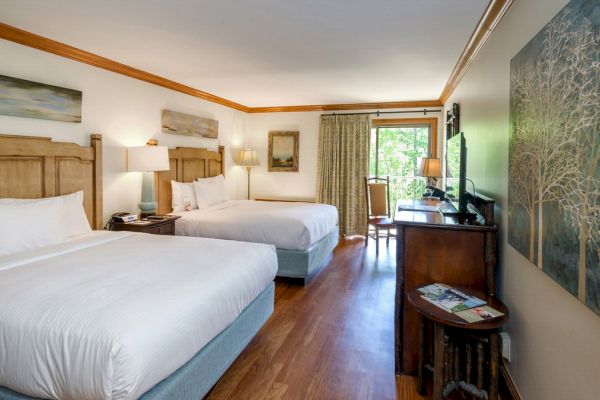 The image shows a hotel room with two beds, wooden furniture, modern decor, a TV, artwork on the walls, and a view of greenery through glass doors.