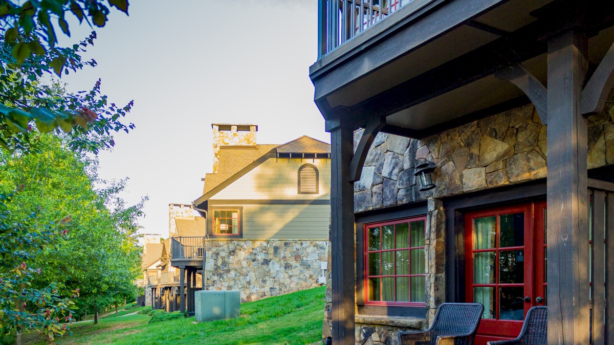 Multiple houses with stone walls, balconies, and outdoor seating areas are shown in a serene, tree-lined neighborhood.