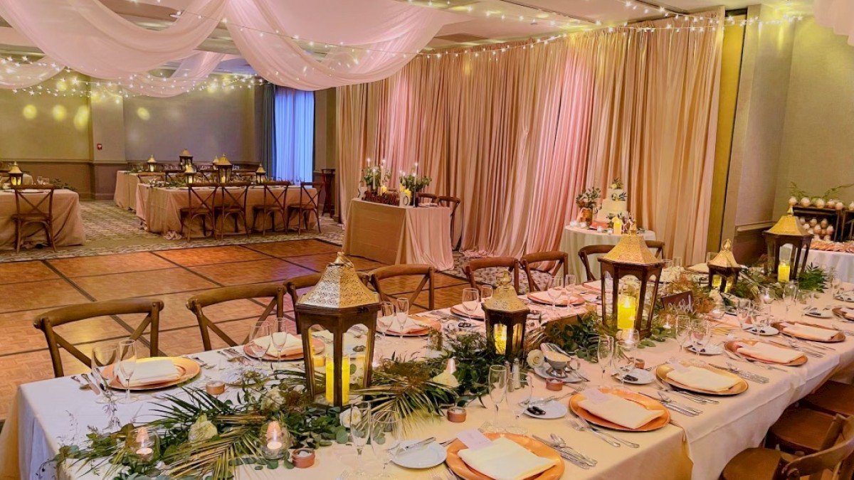 A beautifully decorated wedding reception area with elegant table settings, lantern centerpieces, and soft pink drapery.