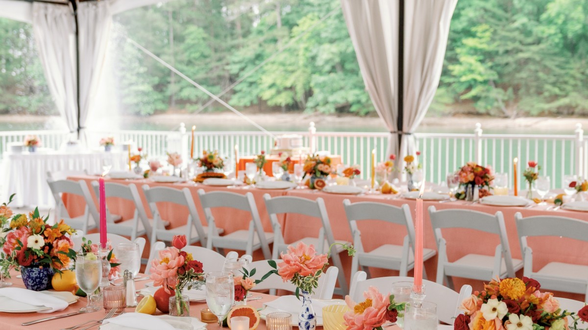 A beautifully decorated outdoor wedding reception with a long pink table, floral centerpieces, candles, and string lights overhead.