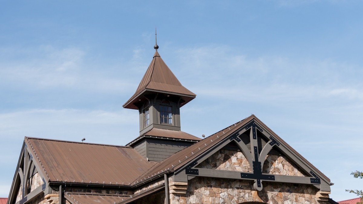 A stone building with a brown roof and small tower, surrounded by plants, with golf carts parked in front under a blue sky.