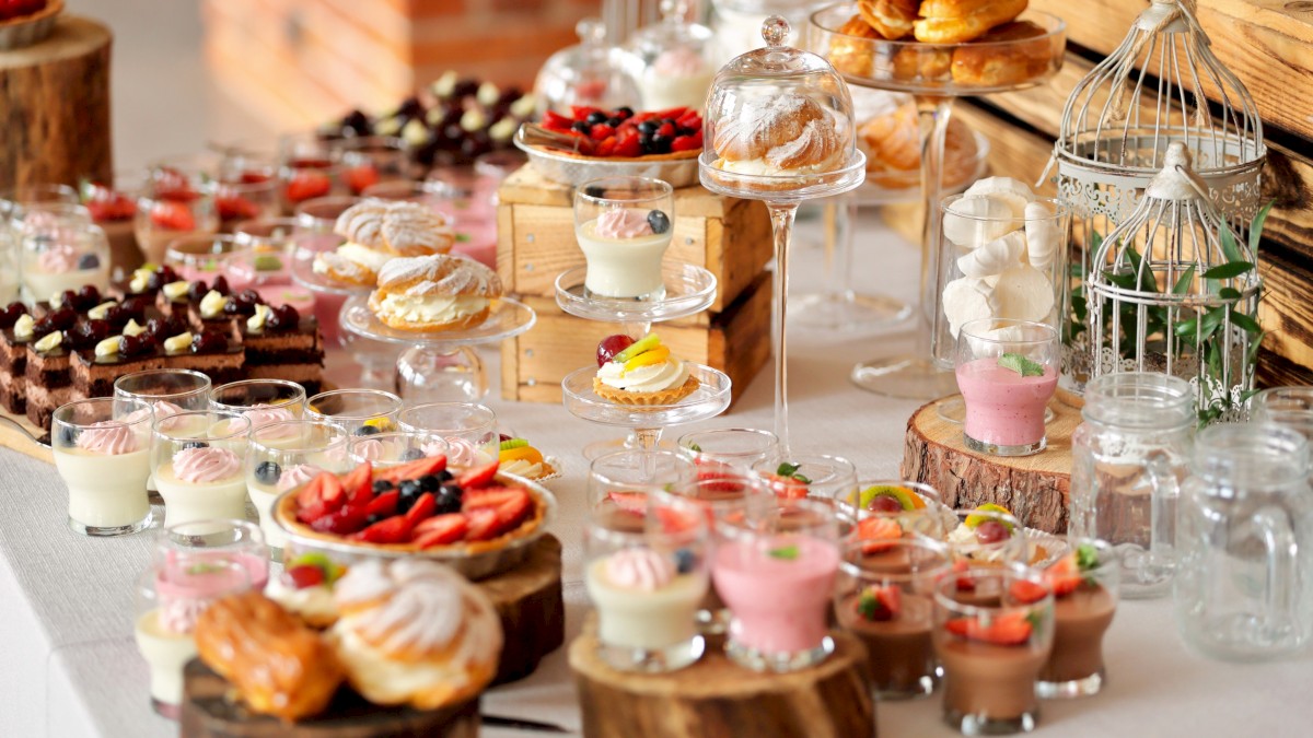 A variety of desserts including tarts, parfaits, éclairs, and fruit snacks arranged on wooden slabs and glass stands at a buffet.