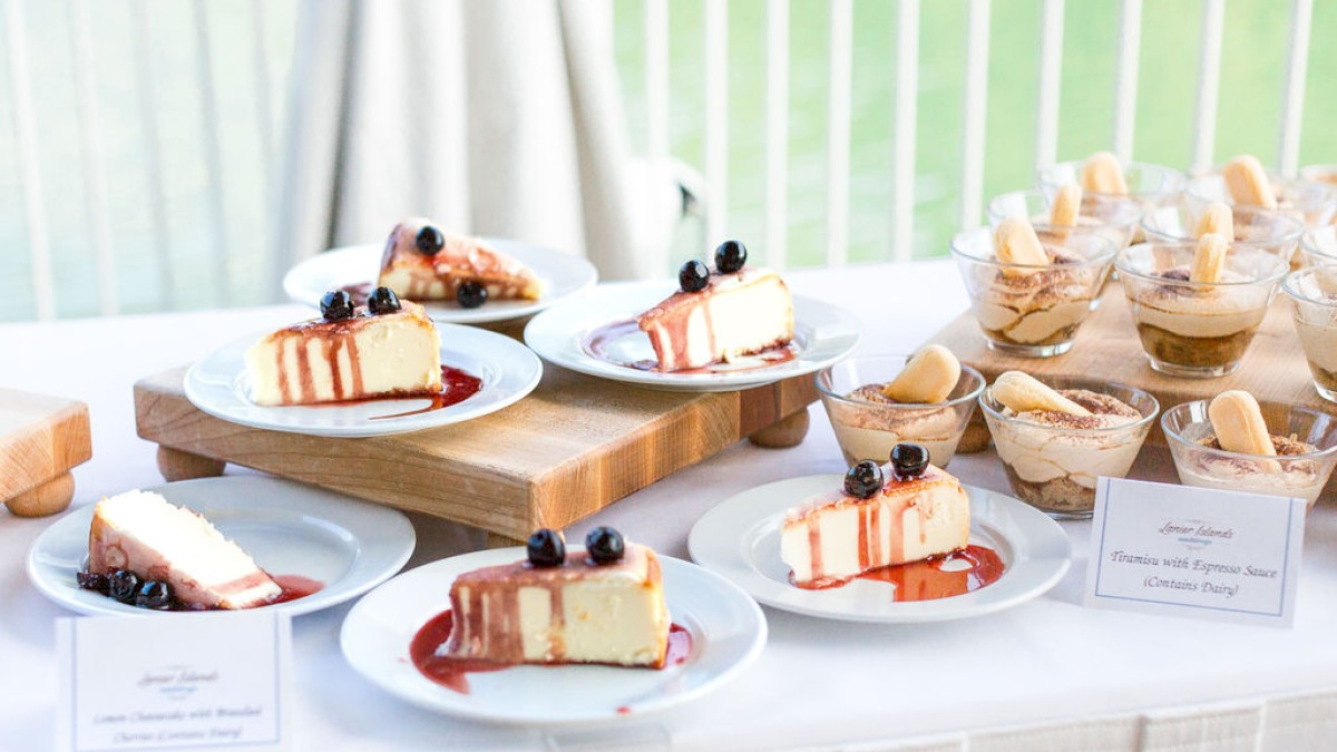 Slices of lemon cheesecake topped with blueberries and drizzled with raspberry sauce are displayed alongside individual desserts with espresso.