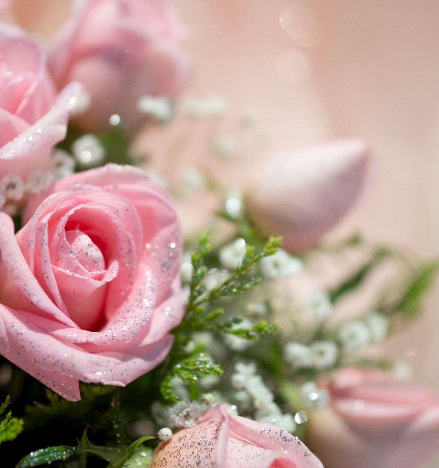 A close-up of pink roses and small white filler flowers with glitter on their petals, creating a soft and romantic floral arrangement.