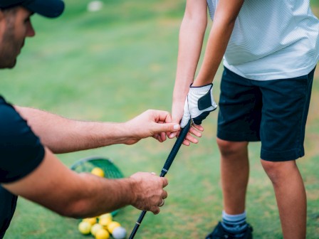A golf instructor helps a young boy with grip and stance during a practice session on the golf course.