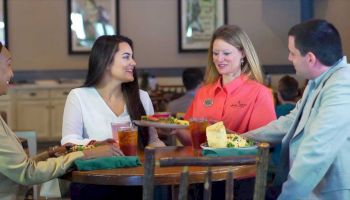 A group of three people at a restaurant conversing as a waitress serves their food and drinks.