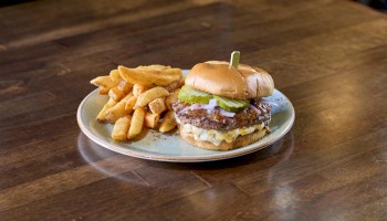 A plate with a cheeseburger, a pickle spear, and a generous side of thick-cut fries on a wooden table.