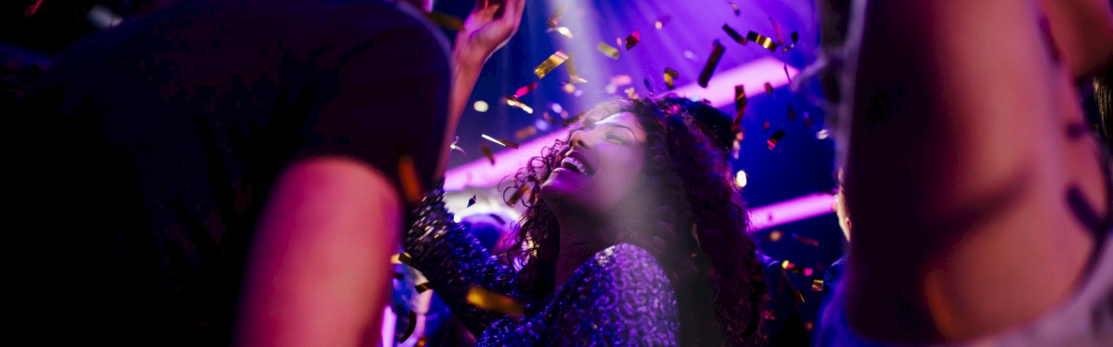 People dancing at a party under colorful lights with confetti flying around.