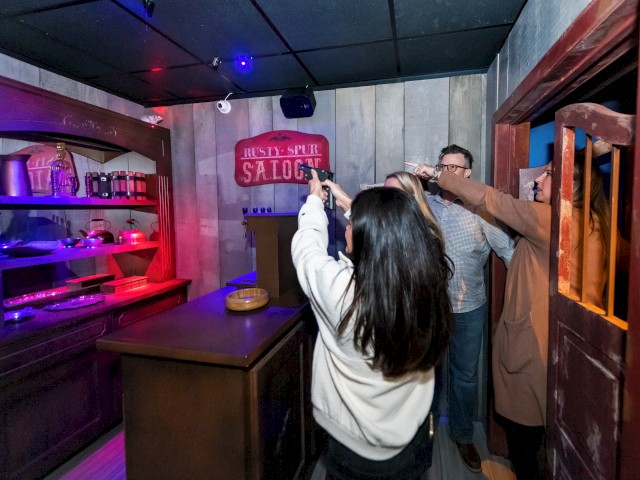 A group of people are pointing guns at each other during an interactive game or activity at the Rusty Spur Saloon.