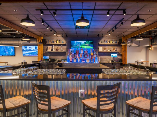 A modern bar with a wooden ceiling, multiple TV screens, and bottles of liquor on shelves behind the bar counter.