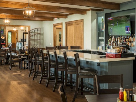 This is an image of a cozy bar area with a TV showing a golf game, wooden furniture, and a well-lit, inviting atmosphere.
