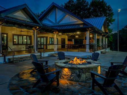 A cozy outdoor fire pit area with four chairs in front of a warmly lit house during dusk.