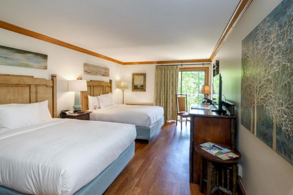 A hotel room with two large beds, a TV on a wooden dresser, wall art, and a window with curtains leading to a balcony or outdoor area.