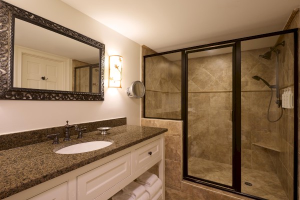 A modern bathroom features a granite countertop, framed mirror, wall light, and a glass-enclosed shower with tiled walls.