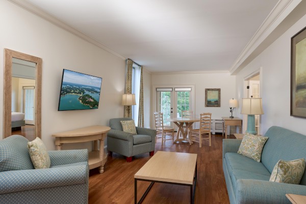 A cozy living room with sofas, armchairs, a coffee table, wall-mounted TV, and a dining area by large windows.