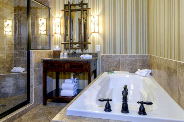 A bathroom with a bathtub, a vanity with a mirror, towels, a shower area with glass doors, and striped wallpaper.