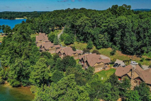 Aerial view of a lakeside community with several houses nestled among trees, and a body of water visible to the left.