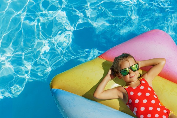 A girl with sunglasses floats on a colorful inflatable in a swimming pool on a sunny day.