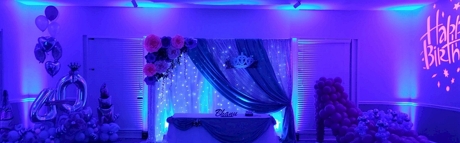A decorated birthday celebration setup with blue lighting, balloons, flowers, and a 