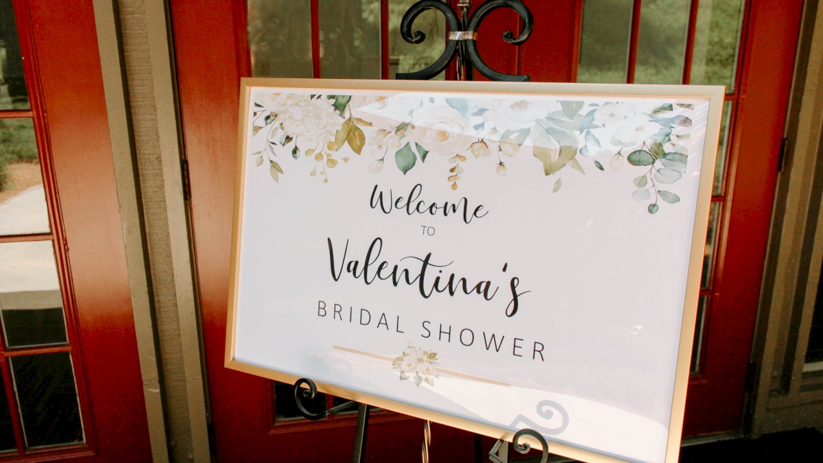 A welcome sign for Valentina's bridal shower, decorated with floral designs, standing in front of a red door.