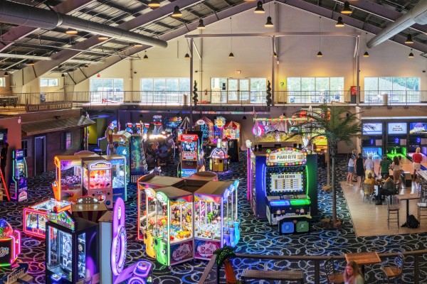An arcade with various games, colorful machines, a snack bar, and a group playing indoor bowling lanes in a spacious, brightly lit hall.