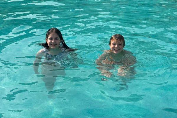 Two kids are smiling and enjoying themselves in a swimming pool on a sunny day.